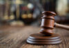 Close-up of a wooden gavel on a wooden surface with blurred scales of justice in the background