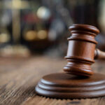 Close-up of a wooden gavel on a wooden surface with blurred scales of justice in the background