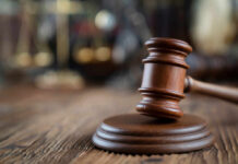 Close-up of a wooden gavel on a wooden surface with blurred scales of justice in the background