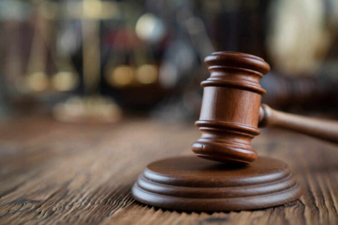 Close-up of a wooden gavel on a wooden surface with blurred scales of justice in the background