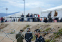 New EU Policy Stirs Refuge Debate Barbed wire fence in front of a refugee camp with people in the background