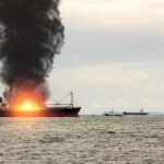 Cargo ship on fire with thick black smoke at sea