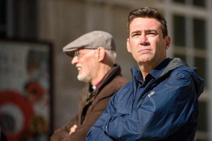 Man in blue jacket standing outdoors with another man in background