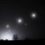 Foggy night landscape with distant lights and silhouetted trees