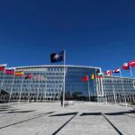 NATO headquarters with member flags in front under a clear blue sky