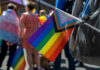 A colorful pride flag held by a participant at a parade, with people in the background