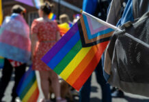 A colorful pride flag held by a participant at a parade, with people in the background