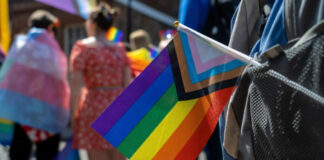 A colorful pride flag held by a participant at a parade, with people in the background