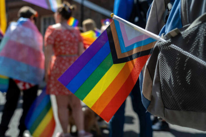 shutterstock_2312590215 A colorful pride flag held by a participant at a parade, with people in the background