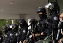 A line of law enforcement officers in riot gear standing ready