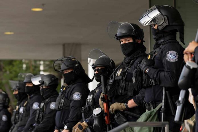 A line of law enforcement officers in riot gear standing ready