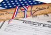 A rolled Declaration of Independence tied with red, white, and blue ribbons next to a birth certificate