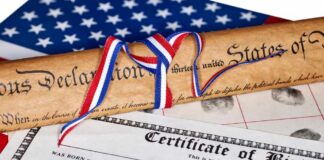 A rolled Declaration of Independence tied with red, white, and blue ribbons next to a birth certificate