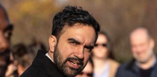 A man speaking passionately at an outdoor event with an engaged audience in the background