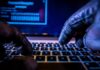 Russian Cyber Pipeline Bleeds U.S. Close-up of gloved hands typing on a laptop keyboard in a dark setting