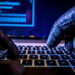 Russian Cyber Pipeline Bleeds U.S. Close-up of gloved hands typing on a laptop keyboard in a dark setting