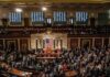 Legislators gather on a chamber floor beneath a large flag