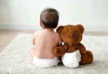 Baby in diaper sitting with teddy bear