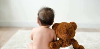 Baby in diaper sitting with teddy bear