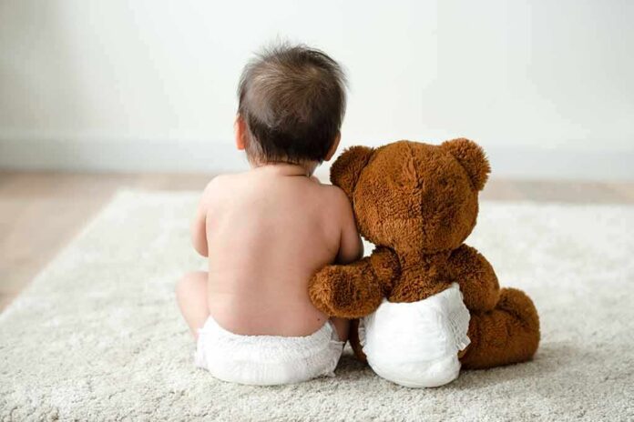 shutterstock_1273839757 Baby in diaper sitting with teddy bear