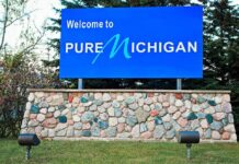 Could El-Sayed’s Auto Plans Cost Michigan? Blue roadside sign on a stone base at a state border