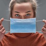 Person holding a blue surgical mask in front of their face
