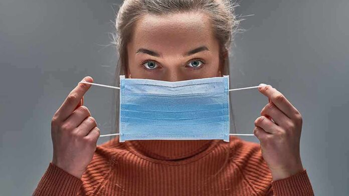 Person holding a blue surgical mask in front of their face
