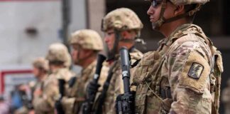 Soldiers in camouflage gear stand in formation holding rifles