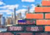 Families First: Politicians Told to Stand Down Brick wall with American flag and memorial text against city skyline
