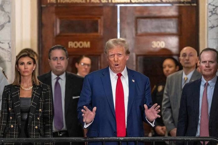shutterstock_2411512537 Man in blue suit speaking to press indoors, flanked by several people