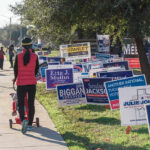 Georgia Pastor Caught In AirTag Sting Person walking with stroller past numerous election campaign signs.