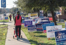 Georgia Pastor Caught In AirTag Sting Person walking with stroller past numerous election campaign signs.