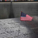 Mamdani And AOC Caught At Ground Zero American flag on a rainy memorial nameplate.