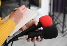 Man Survives Two Hours Inside Garbage Truck Journalist holding two microphones while writing in a notebook