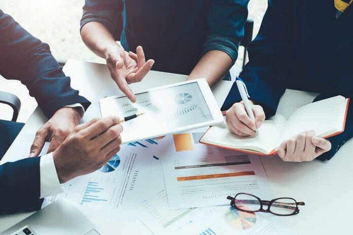 shutterstock_1020878011 Business meeting with hands pointing at tablet and taking notes