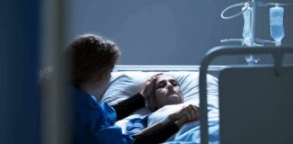 Patient in hospital bed with visitor holding their hand
