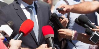 Trump Bars CNN, Politico – What’s Next? Person in suit surrounded by microphones during media interview