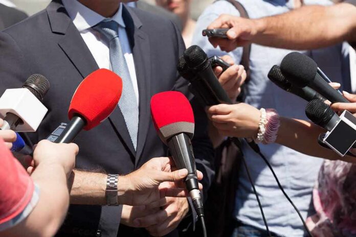 shutterstock_1042717348 Person in suit surrounded by microphones during media interview