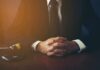 X-Rated Scandal Ousts Teenage Mayor person in suit with hands clasped at a desk beside a gavel