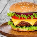 Cheeseburger with lettuce, tomato, and onion on a wooden plate