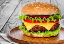 Mass Closures Hit Wendy’s Nationwide Cheeseburger with lettuce, tomato, and onion on a wooden plate
