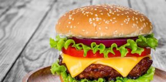 Mass Closures Hit Wendy’s Nationwide Cheeseburger with lettuce, tomato, and onion on a wooden plate