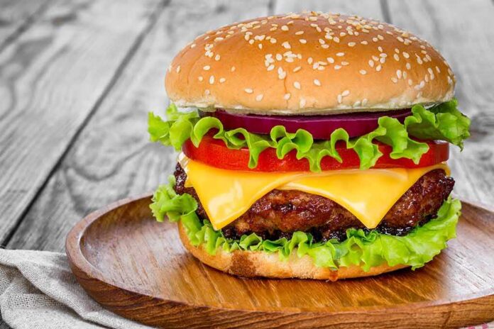 Cheeseburger with lettuce, tomato, and onion on a wooden plate
