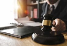 Judge's gavel on desk with person reading documents in background