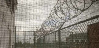 Power Clash Erupts Over ICE Site Barbed wire on chain-link fence at a prison yard
