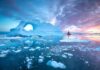 Iceberg with arch and red-sailed boat at colorful sunset
