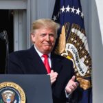 Future Alliance Taunts Draw Trump Fire man in suit clapping at a podium with presidential seal
