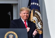 man in suit clapping at a podium with presidential seal