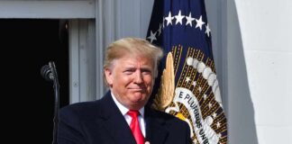 man in suit clapping at a podium with presidential seal