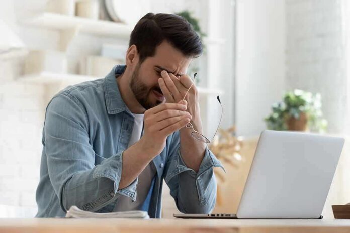 Man rubbing eyes while holding glasses at a laptop